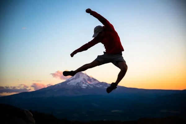 Energy Boost - man leaping into air in front of mountain